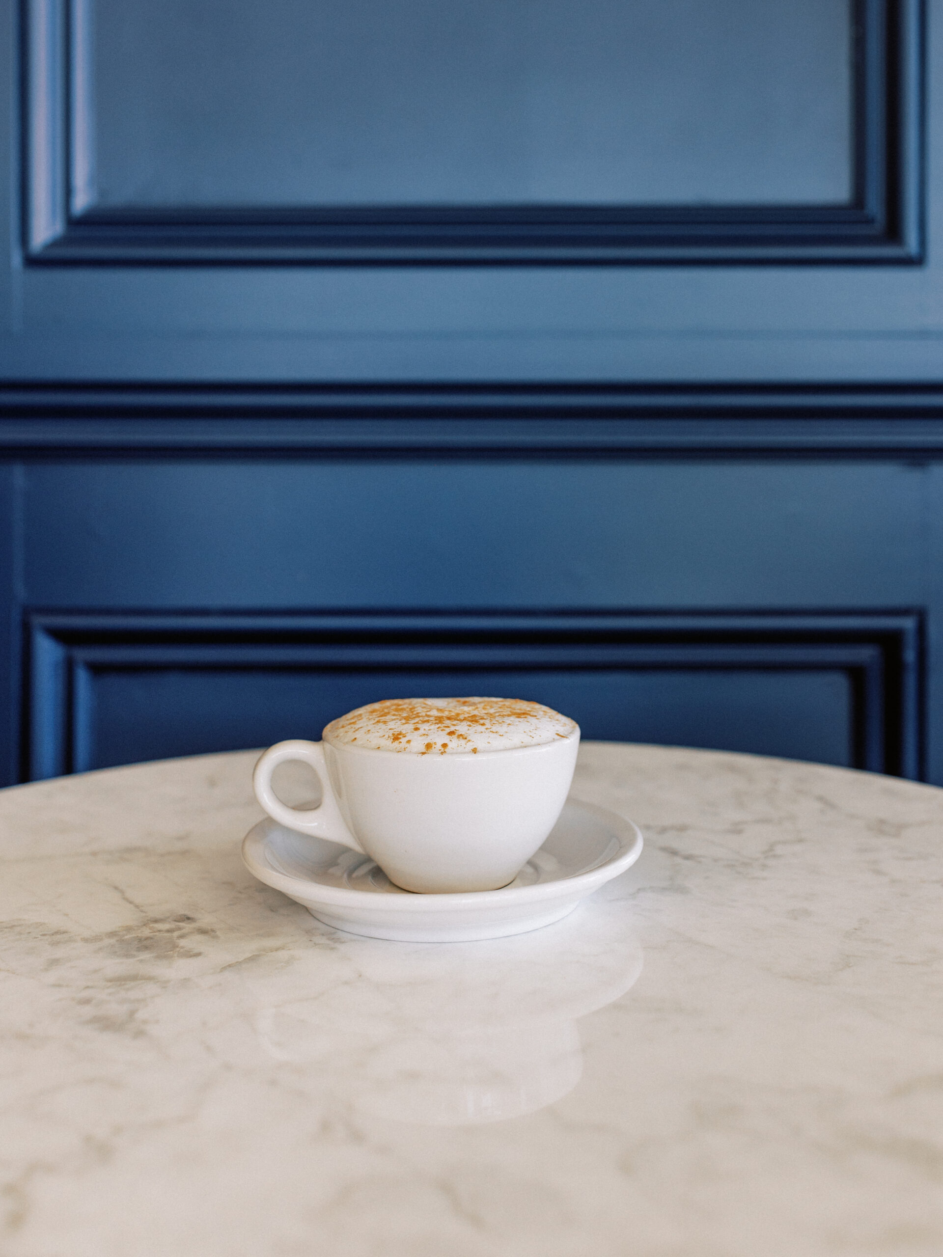 Cappuccino with foam art on marble table against navy paneled wall at Avenue Brew