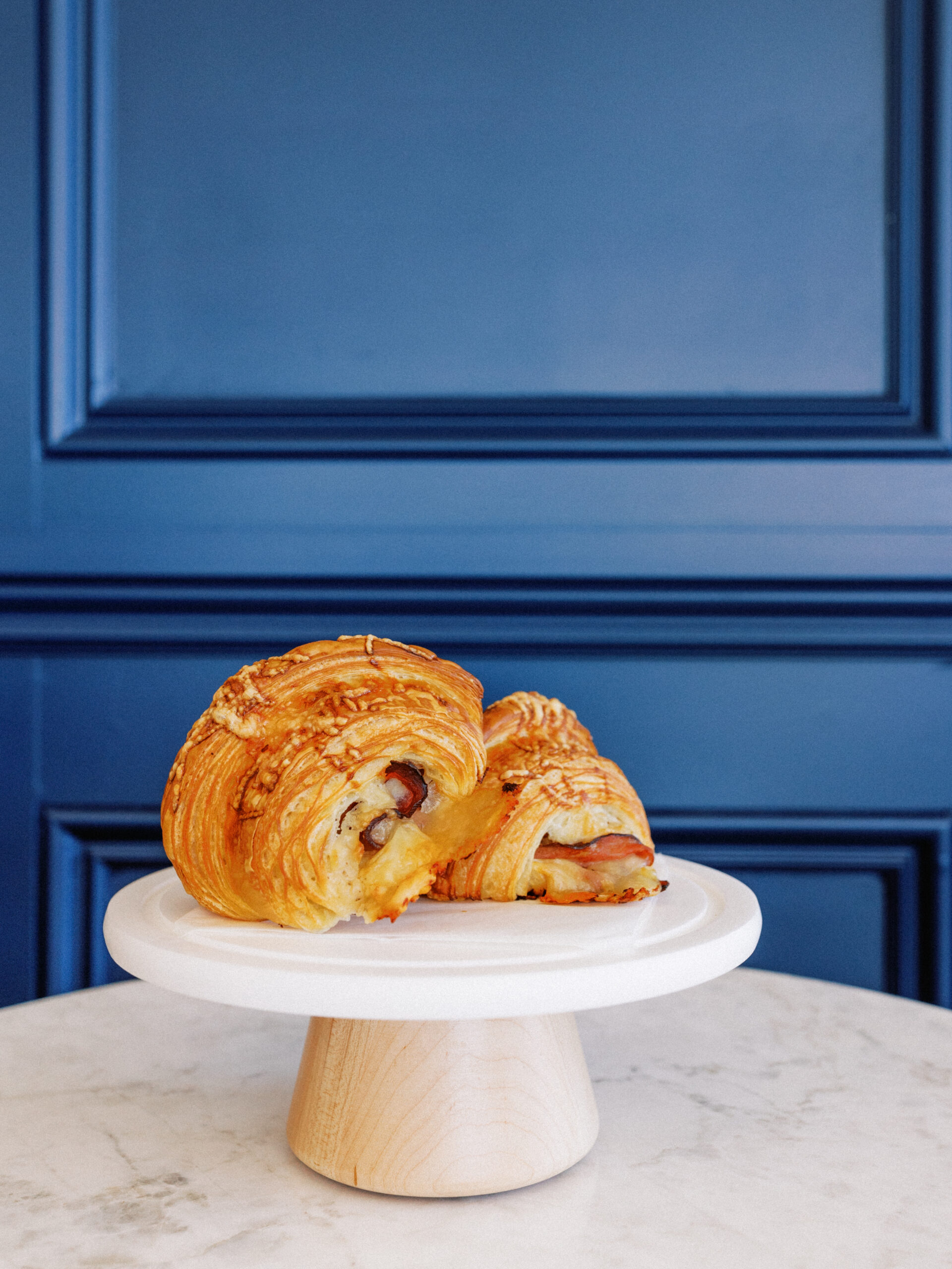 Fresh-baked ham and cheese croissant on wooden cake stand at Avenue Brew